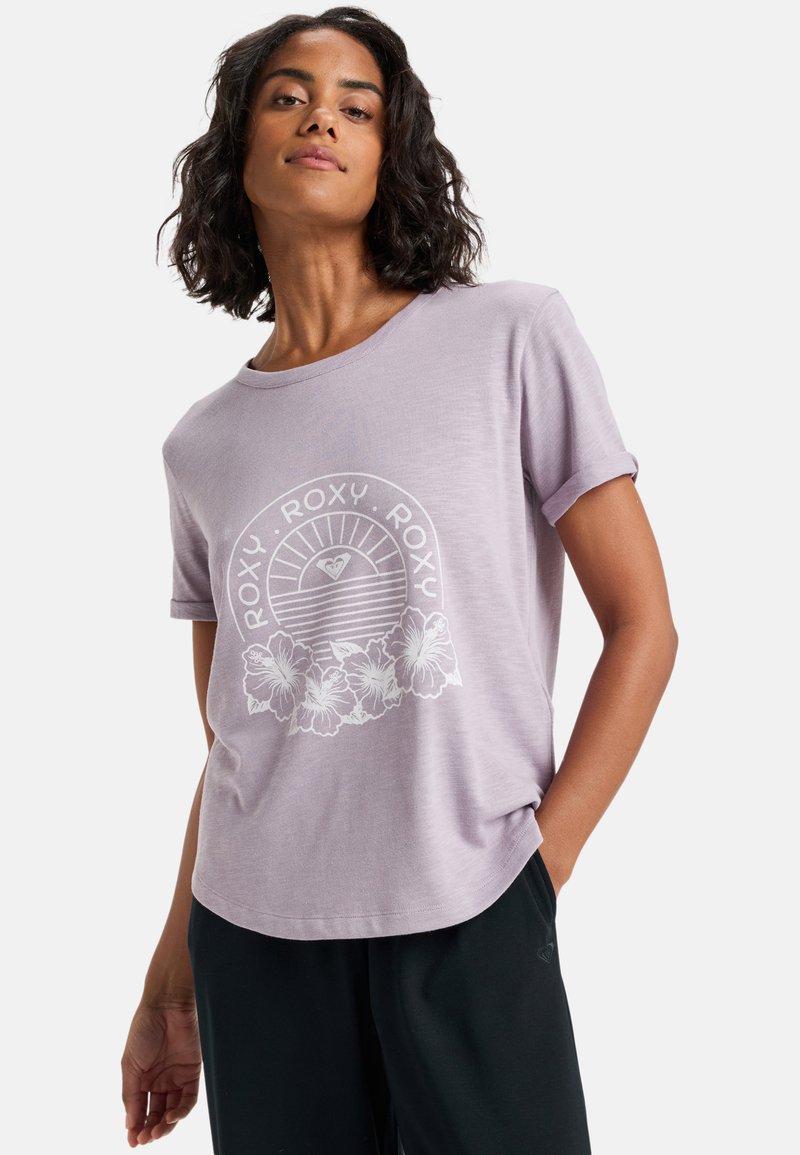 Camiseta de manga corta en color lila de tela suave, presenta un gráfico blanco con texto y un diseño floral. Corte relajado con un escote redondeado.