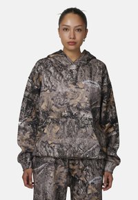 Felpa camouflage nelle tonalità di marrone e grigio, con tasca frontale e cappuccio regolabile con cordino. Decorata con un logo in bianco sul petto.