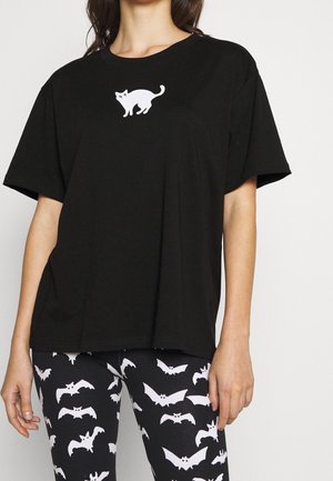 Black oversized t-shirt with a small white scared cat print on chest, paired with black leggings covered in white bat patterns.
