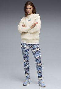 Crèmekleurige sweatshirt met subtiele logo, gecombineerd met blauwe legging met bloemendessin en witte accenten. Lichtblauwe sneakers maken de look compleet.