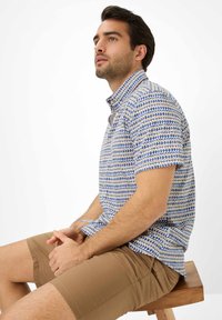 Camicia a maniche corte con un motivo geometrico blu e beige, realizzata in tessuto leggero. Presenta un colletto abbottonato e una vestibilità rilassata.
