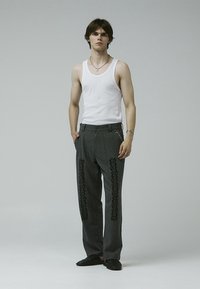 Gray patterned trousers with black embroidery along the sides, paired with a white tank top and black slip-on shoes. Minimalistic style.