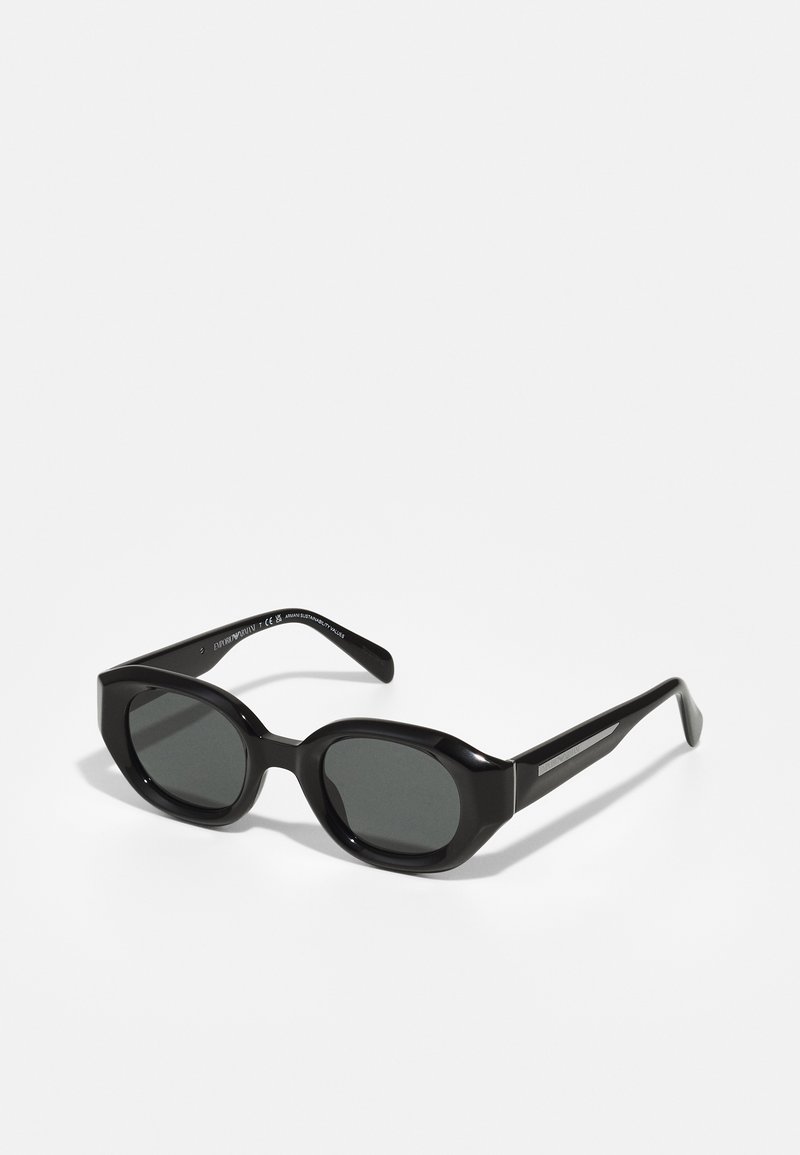 Ochelari de soare din plastic negru, cu lentile ovale, rame groase și tempere elegante, cu accente metalice subtile. Finisaj mat cu o textură netedă.