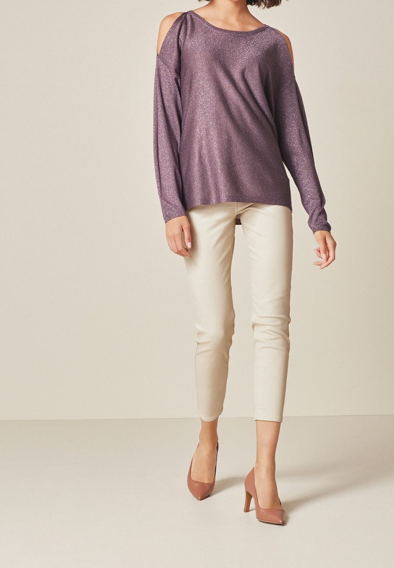 Purple glitter long-sleeve top with cut-out shoulders, paired with fitted beige pants and light brown high heels. Smooth texture, relaxed fit.