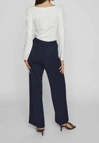 Vit långärmad topp med vid halsringning, i kombination med marinblå vida byxor med elastisk midja och bakfickor. Svarta klacksandaler.