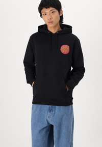 Črna kapuca s sprednjim kenguru žepom, kapuco na vrvico in rdečim grafičnim logotipom. Narejena iz mehkega materiala; ima rebraste manšete in spodnji rob.