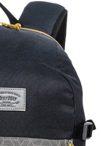 Schwarzer Stoffrucksack mit strukturierten Oberflächen, grauem Musterboden, gelbem Reißverschluss-Zipper und einem weißen Etikett mit "Rest Way"-Branding.