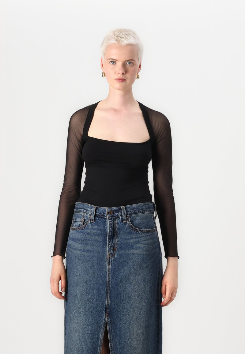 Schwarzer langärmliger Body mit einem quadratischen Ausschnitt, kombiniert mit einem hochgeschnittenen Jeansrock mit einem Schlitz vorne und klassischem Knopfverschluss.
