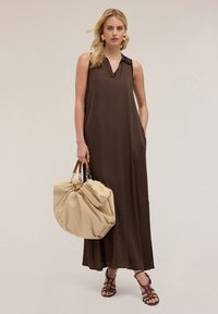 Rochie maxi fără mâneci, de culoare maro, cu decolteu în V, buzunare laterale și țesătură fină. Asortată cu o geantă mare bej și sandale negre cu bretele.