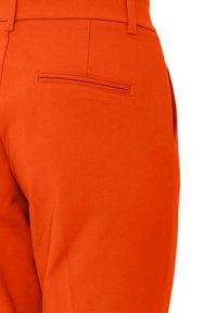 Un pantalon orange vif en tissu lisse, doté d'une poche arrière avec un détail de couture horizontale. Le design met en avant une coupe ajustée.