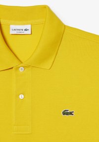 Polo shirt Lacoste giallo con vestibilità classica, caratterizzato da un tessuto testurizzato, collo con tre bottoni e logo coccodrillo verde ricamato.