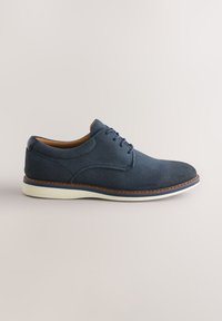 Chaussure décontractée en daim bleu marine à lacets avec semelle blanche et bordure marron cousue, vue de côté sur un fond uni.