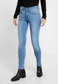 Ljusblå skinny jeans i denim med hög midja, framfickor och knappstängning, parat med svarta ankle boots.