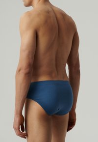 Męskie niebieskie slipy wykonane z miękkiego materiału, z subtelnym wzorem, elastycznym pasem i dopasowanym krojem. Brak widocznej marki.