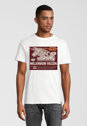 Weißes Baumwoll-T-Shirt mit einer Grafik des Millennium Falcon, versehen mit roten und cremefarbenen Text, der Details und Designelemente des Maßstabsmodells zeigt.