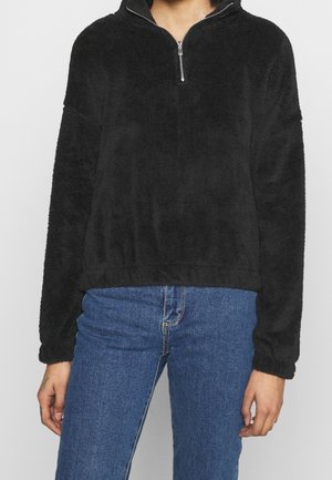 Sort fleece pullover med halvlange lynlås, lange ærmer og et blødt, struktureret stof. Den cropped længde sidder over højtaljede jeans.