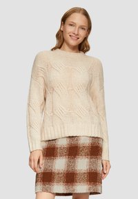 Cremfarbener Strickpullover mit Kabelmuster, runder Halslinie und geripptem Saum, kombiniert mit einem karierten Rock in Braun und Creme.