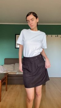 Svart skjørt med høy midje, sidelommer og knappestenging. Kombinert med en enkel hvit t-skjorte. Glatt tekstur, avslappet design.