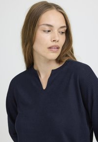 Navyblaues Pullover mit V-Ausschnitt, gerippten Details an den Ärmeln und einem strukturierten Strickmuster. Eignet sich für die Freizeit.