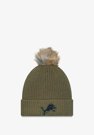 Olivgrüner gestrickter Beanie mit umgeschlagenem Bündchen, der oben einen Kunstfell-Pom-Pom und ein dunkles Emblem eines Löwen auf der Vorderseite zeigt.