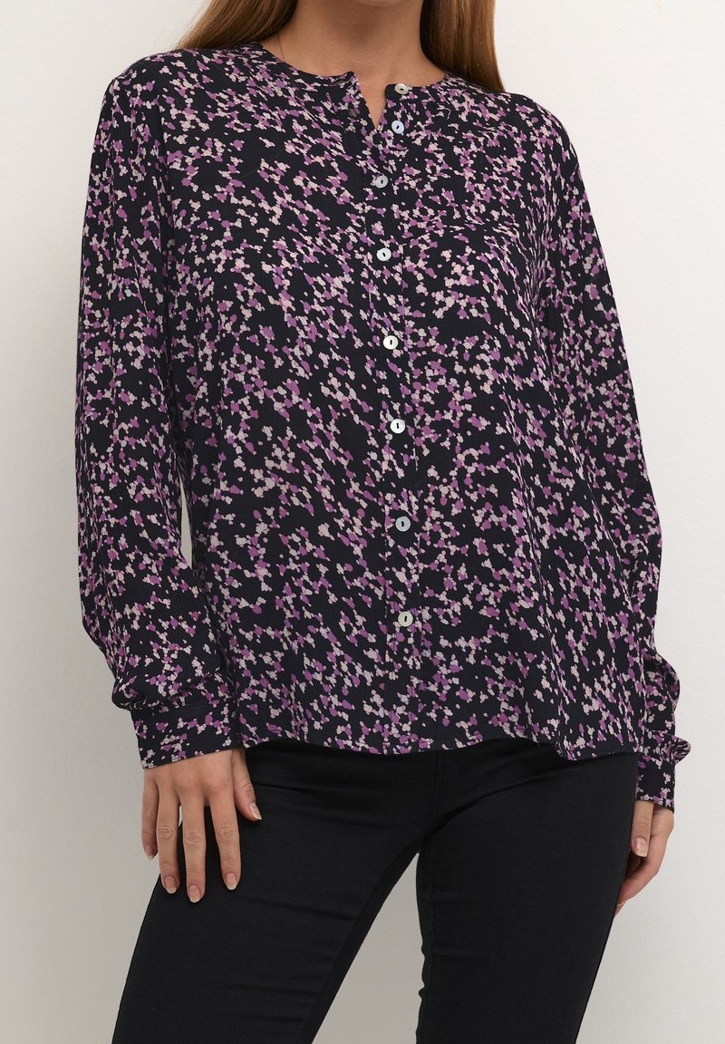 Knap-bluse i navy med blomstermønster i lilla og pink. Lange ærmer med knapmanchetter. Letvægts, tekstureret stof.