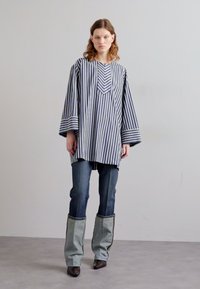 Tunique rayée en navy et blanc avec un col en V, des manches larges ; associée à un jean en denim taille haute avec des accents bleu clair contrastants.