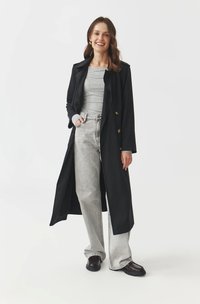 Black long coat with double-breasted gold buttons, gray long-sleeve top, light gray wide-leg jeans, and dark loafers, against a white background.