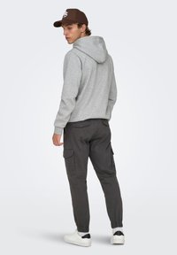 Sudadera con capucha de forro polar gris con cordón, combinada con pantalones cargo negros con bolsillos laterales y zapatillas blancas con detalles en negro.