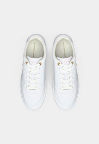 Un paio di sneakers bianche Tommy Hilfiger con lacci e occhielli dorati, viste dall'alto su uno sfondo bianco.