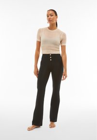 Top corto de punto beige con mangas cortas, combinado con pantalones negros de cintura alta que cuentan con tres botones dorados y un diseño de pierna acampanada.