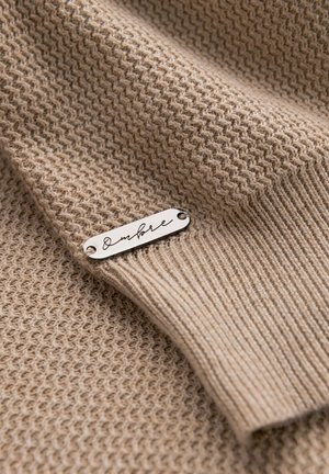 Beige breigoed met een textuurweef en een gladde ribbelrand. Inclusief een zilveren label gegraveerd met "Ombre."