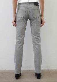 Jeans de denim gris con un corte ajustado, bolsillos traseros y una textura suave, complementados por una cinturilla negra y un dobladillo a la altura del tobillo.