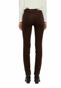 Pantalon en velours côtelé marron à coupe slim, doté de deux poches arrière et d'une ceinture. Porté avec des bottes à talons noires.