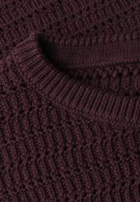 Gros plan d'un pull en tricot violet foncé plié montrant un col côtelé et un motif tricoté texturé.