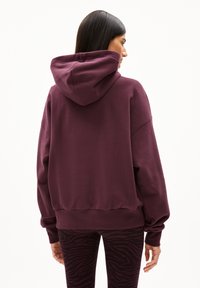 Overmaatse bordeauxrode hoodie met een capuchon, geribbelde mouwen en onderrand, gecombineerd met zwarte leggings met een paars zebra patroon.