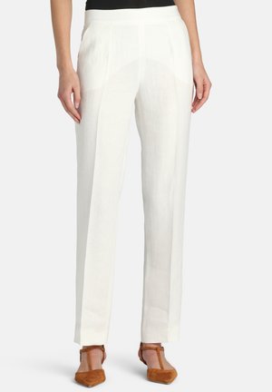 Biele priliehavé nohavice s rovnými nohavicami nosené s hnedými lodičkami s T-ramienkom a špicatou špičkou na osobe s rukami uvoľnene visieť pozdĺž bokov.