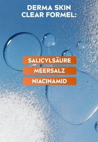 Blue background with liquid droplets and white powder highlighting the ingredients salicylsäure, meersalz, and niacinamid.