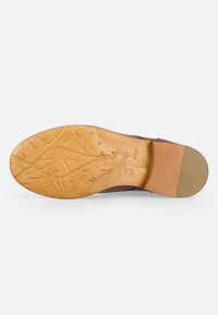 Suela de zapato de cuero marrón con goma texturizada en color beige, presentando patrones en relieve y un toque de tacón de madera.