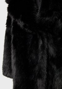 Gros plan sur un tissu en fausse fourrure noire douce avec des fibres denses et brillantes et une texture lisse.