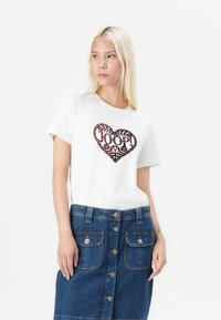 T-shirt alb din bumbac cu un grafic în formă de inimă de culoare vișinie, prezentând flori și textul "JOOP!", asociat cu o fustă din denim albastră cu nasturi.