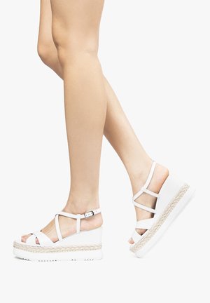 Białe platformowe sandały z plecionymi akcentami z juty, z krzyżującymi się paskami i zapięciem na klamrę, na neutralnym tle.