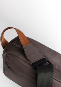 Grau gefärbte Stofftasche mit strukturierten Oberflächen, ausgestattet mit einem orangefarbenen Griff und einem schwarzen verstellbaren Tragegurt. Mit einem Reißverschluss oben und einer robusten Bauweise.