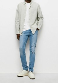 Cotton striped button-up shirt in green and white, layered over a white t-shirt. Light blue skinny jeans and white sneakers complete the look.