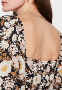 Blumenkleid aus schwarzem Stoff mit weißen und rosa Blumen, Rückenausschnitt, geraffte Details und strukturierte Oberfläche.