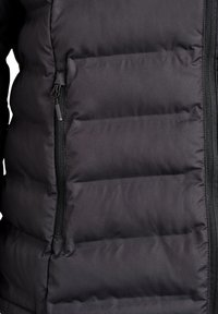 Mustast polsterdatud jakk, millel on tõmblukuga sulgemine, tikitud tekstuur ja küljetasku. Kangas on siledapinnaline ja pehme läikega.