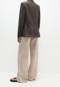 Blazer gris sur mesure avec un design structuré, associé à un pantalon large beige. Texture de tissu lisse et lignes épurées créent une coupe moderne.