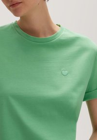 Groene katoenen t-shirt met een ronde hals en korte mouwen, voorzien van een lichtgroene hartborduursel op de linkerborst.