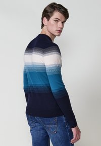 El pulóver de punto presenta rayas degradadas en tonos de azul, gris y blanco, que transición hacia una parte inferior en azul marino; con cuello redondo y un diseño ajustado.