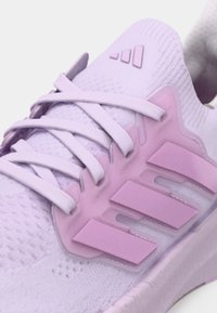 Jasnofioletowy but sportowy z teksturowaną tkaniną na cholewce, wzmocnionym noskiem, płaskimi sznurowadłami oraz trzema fioletowymi paskami po bokach.