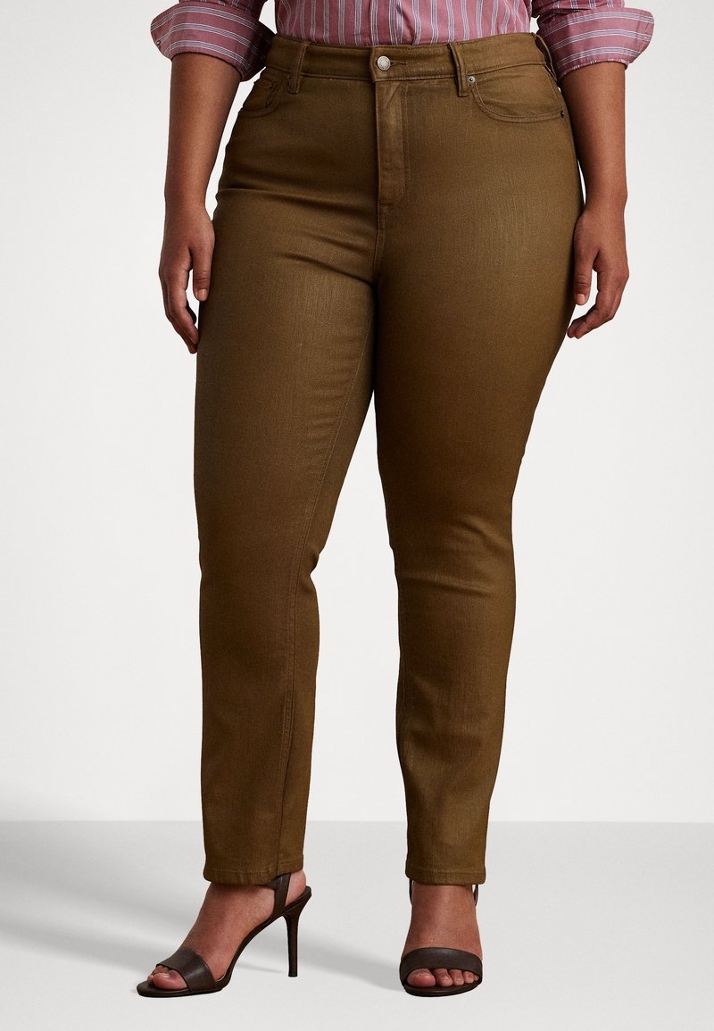 Personne aux courbes portant un pantalon marron slim taille haute, une chemise rose à rayures aux manches retroussées, et des talons ouverts marron foncé.